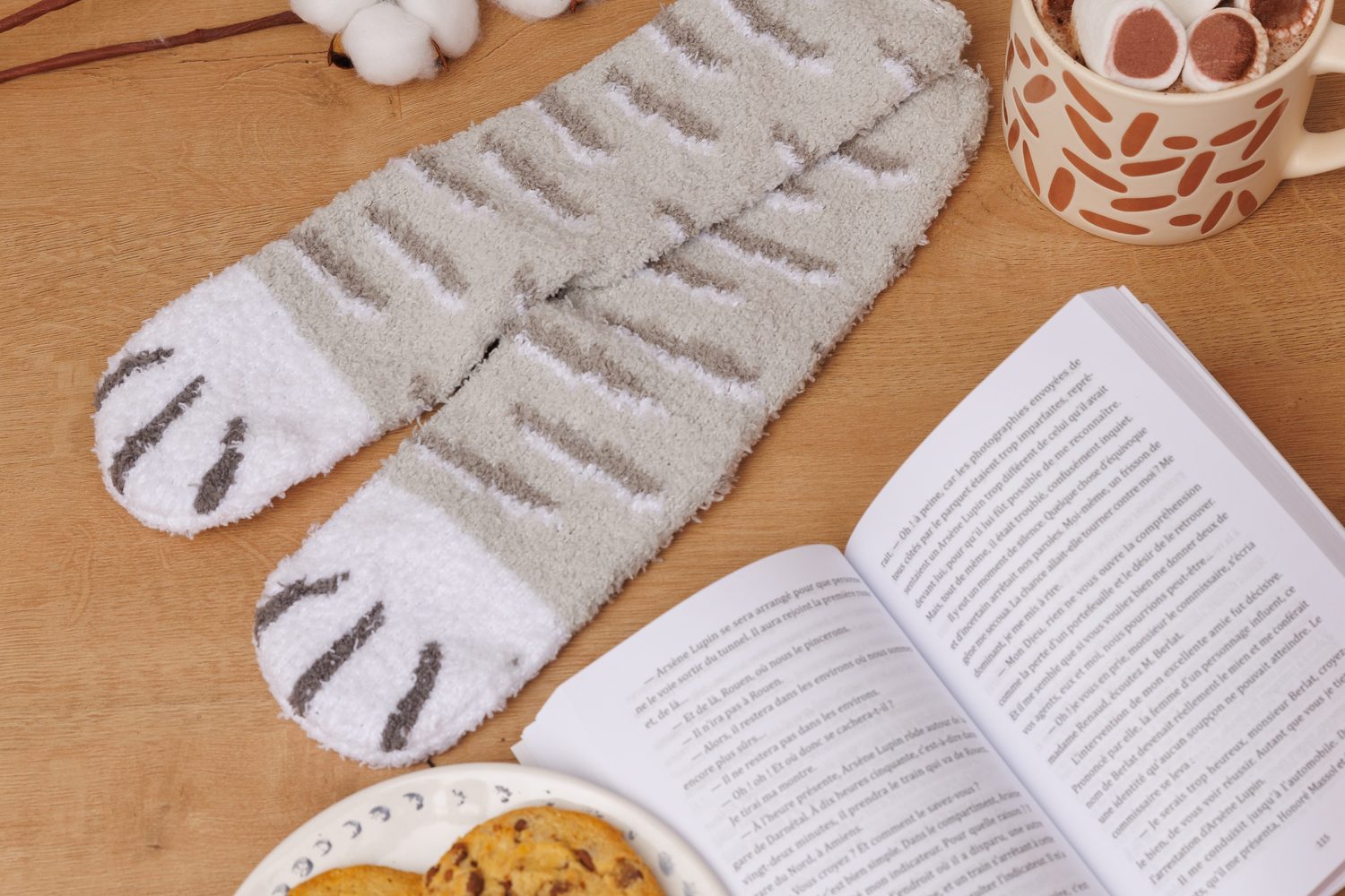 Grey cat paw socks next to cookies, a hot chocolate and an open book