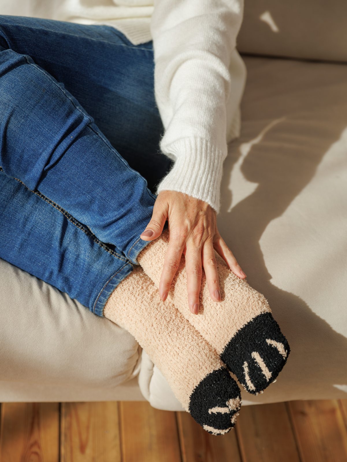 A woman's hand resting on a beige cat paw sock, on a sofa
