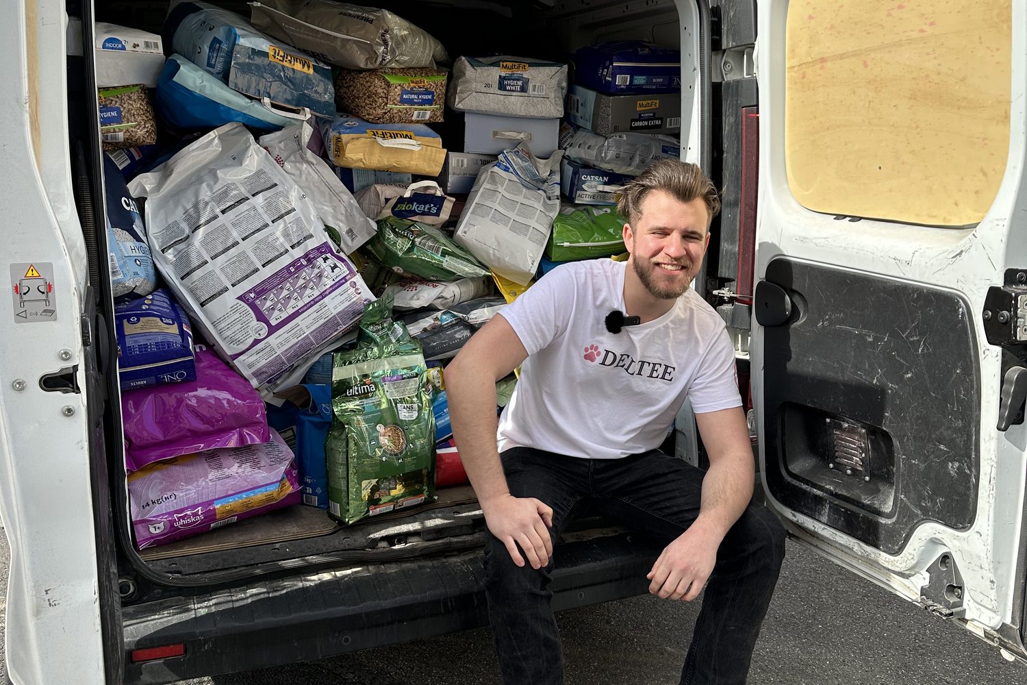 A member of the Deltee team sitting in the back of a van packed with bags of cat food